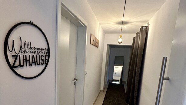 A hallway with a black circular sign on the wall, a carpeted floor, and a light fixture.