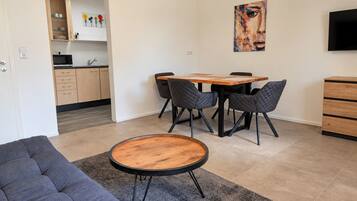 Ein moderner Wohnraum mit einer Couch, einem runden Couchtisch, einem Esstisch mit Stühlen, einer Küchenzeile und einem Bild an der Wand.