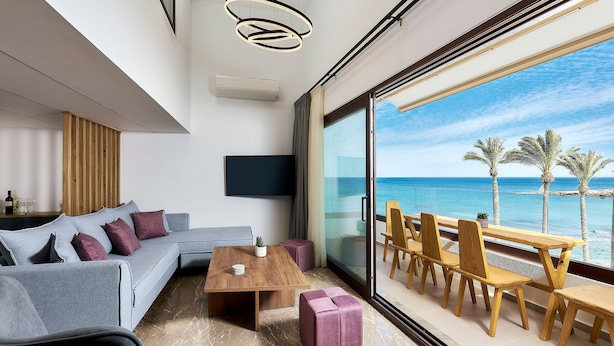 Un salon moderne avec une grande fenêtre donnant sur la mer, une table en bois et un canapé gris.