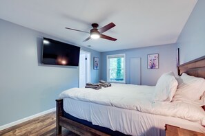 Ein Schlafzimmer mit einem Bett, einem Deckenventilator, einem an der Wand montierten Fernseher und einem Fenster mit Blick auf Bäume.