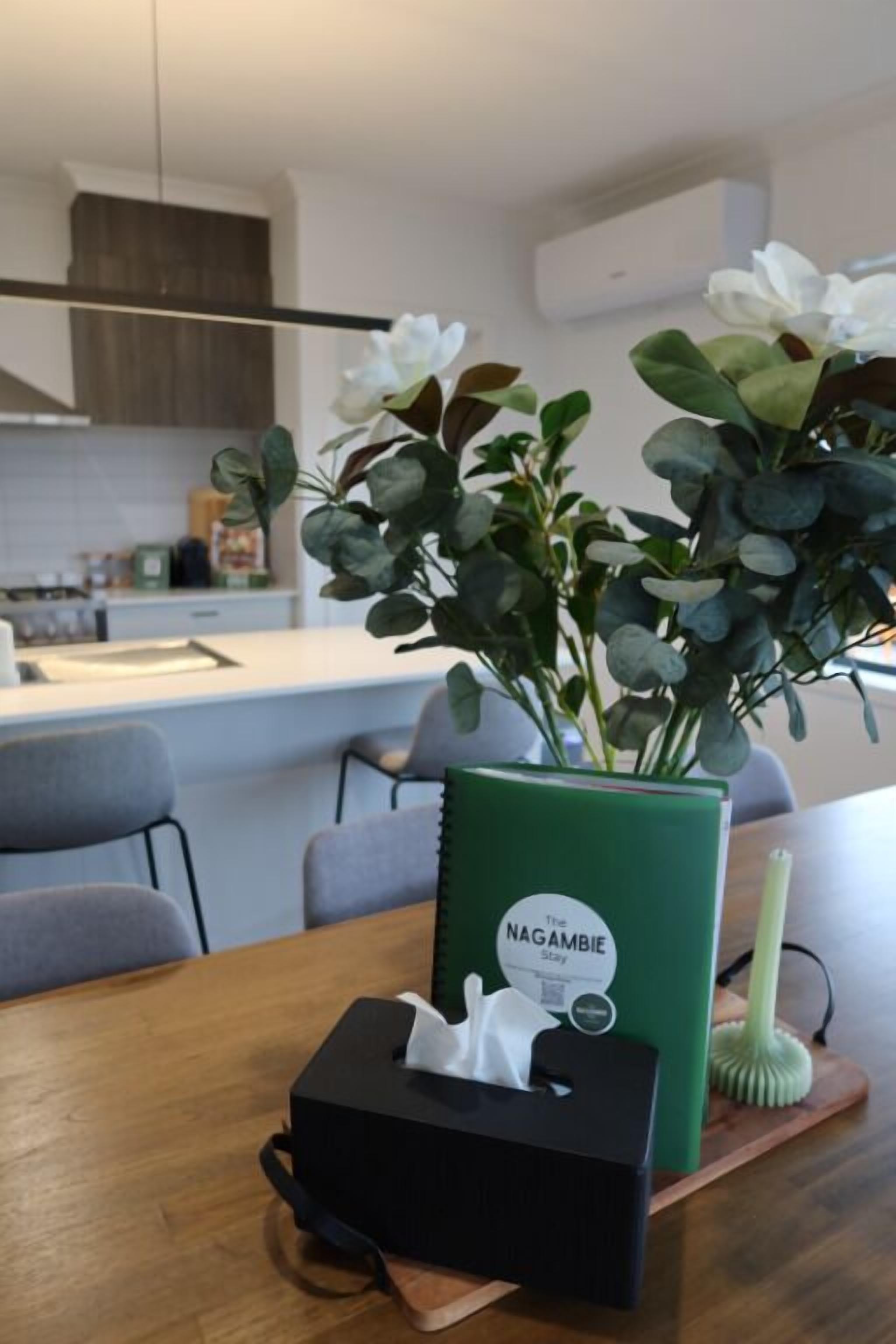 Een moderne keuken met een houten tafel, een groene vaas met witte bloemen, en een zakdoos.