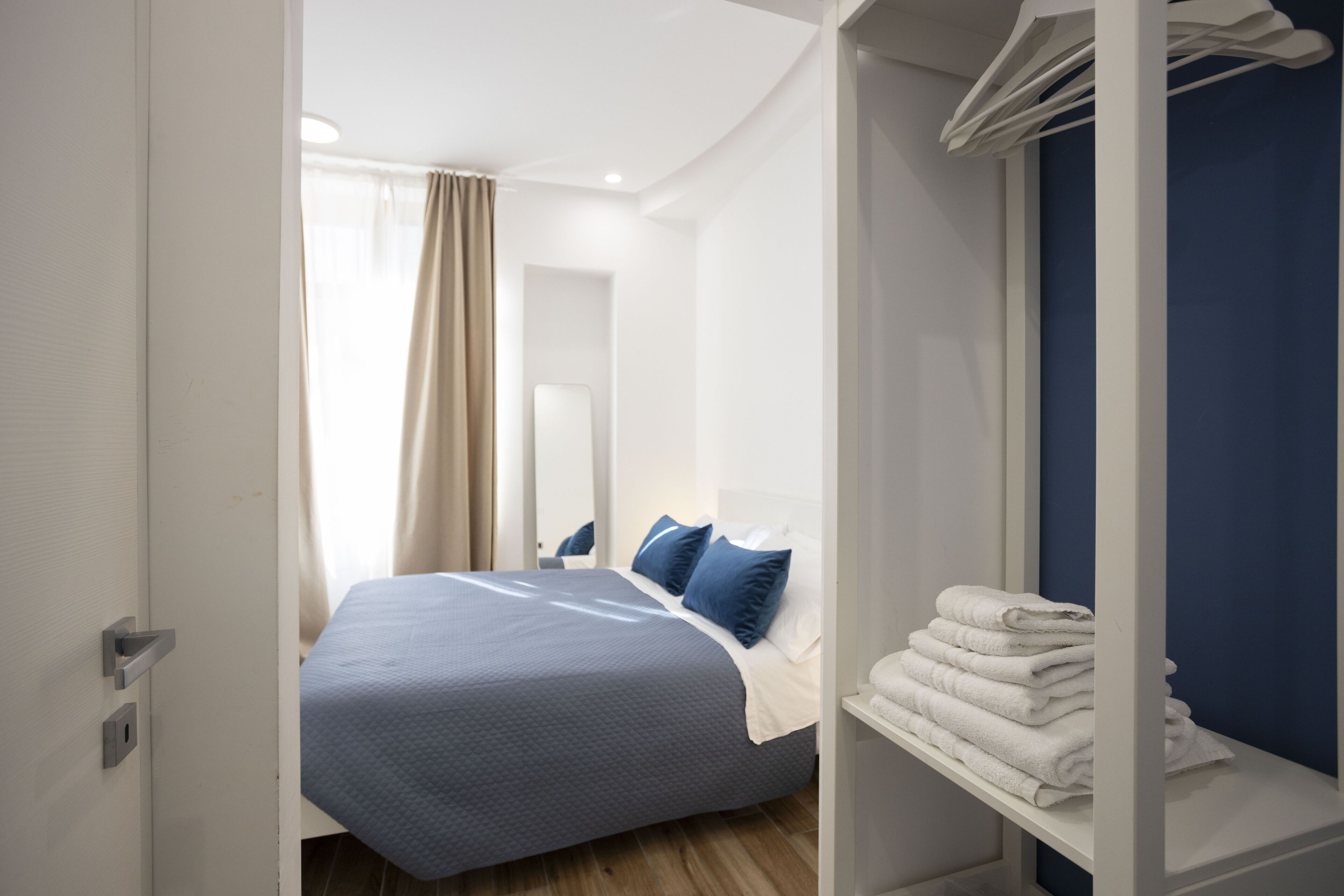 A modern hotel room with a neatly made bed, a bathroom with a towel rack, and a view of the hallway.