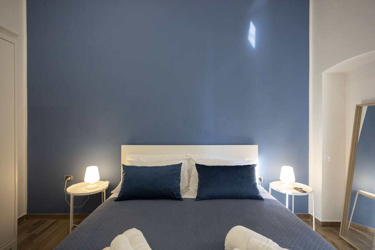 A bed with a white headboard, two bedside tables with lamps, and dark blue walls.