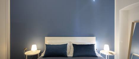 A bed with a white headboard, two bedside tables with lamps, and dark blue walls.