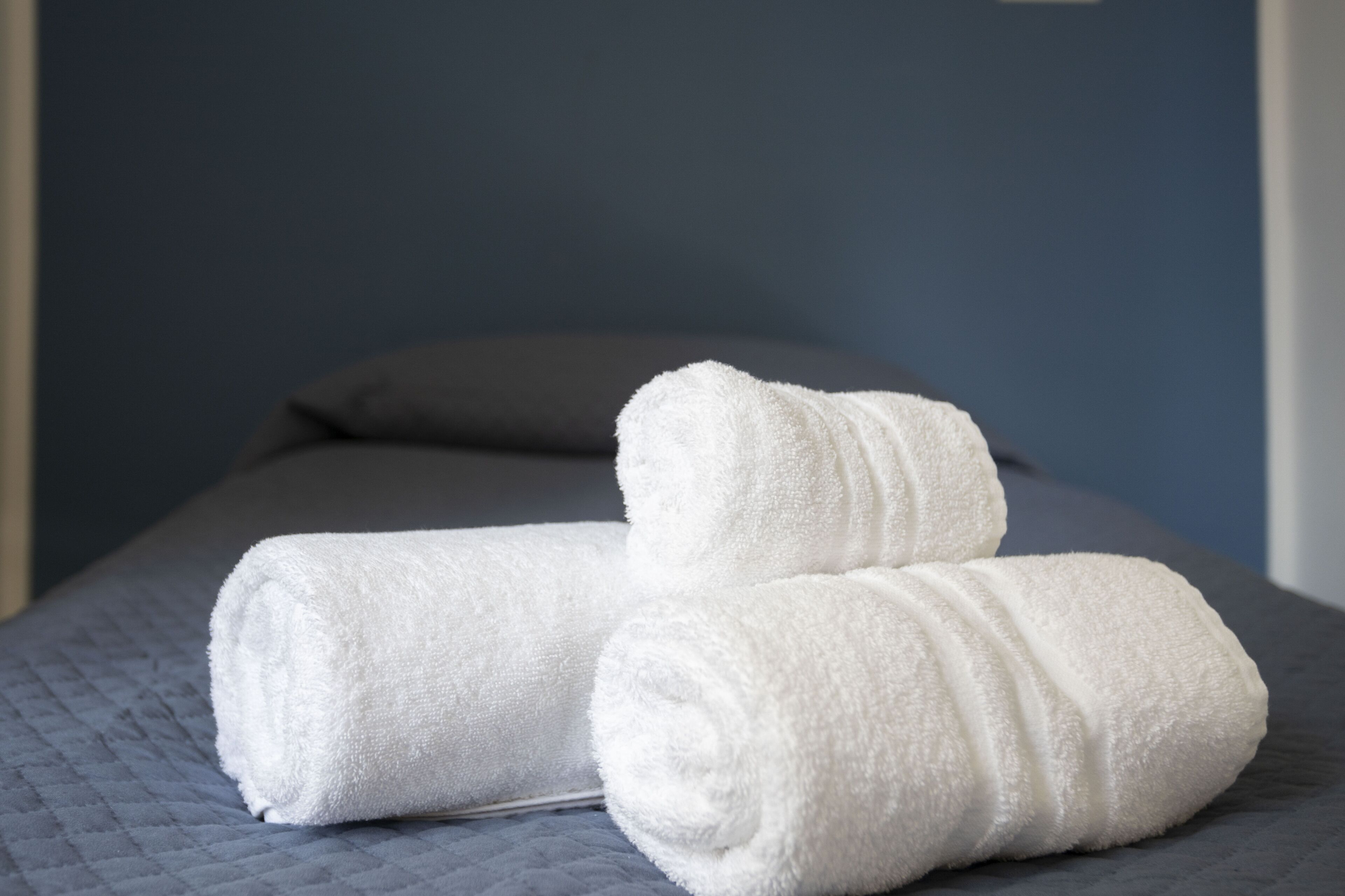 A bed with a quilted gray bedspread and two rolled white towels.