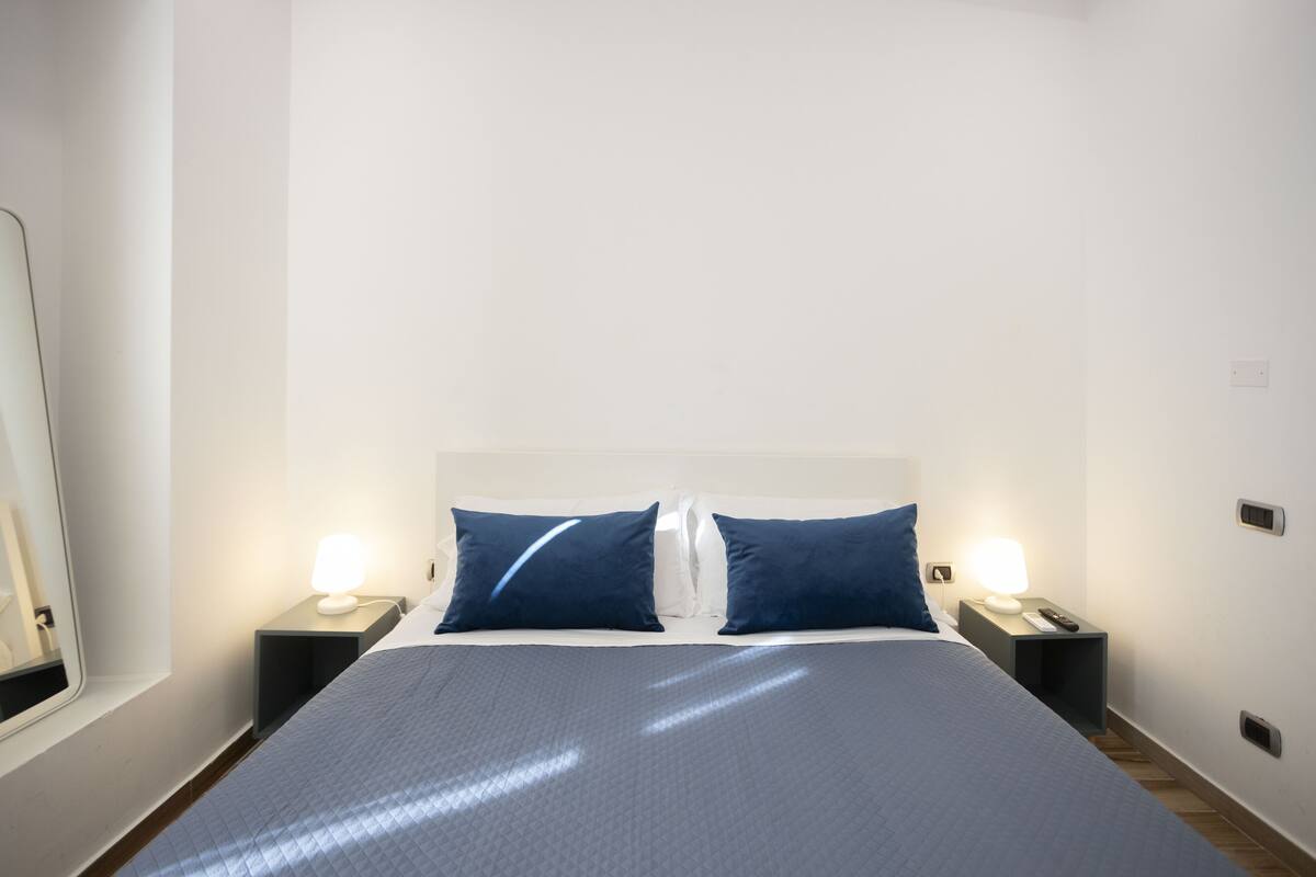 A hotel room with a large bed, two bedside tables with lamps, and a mirror on the left wall.