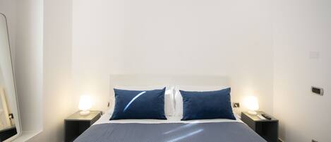A hotel room with a large bed, two bedside tables with lamps, and a mirror on the left wall.