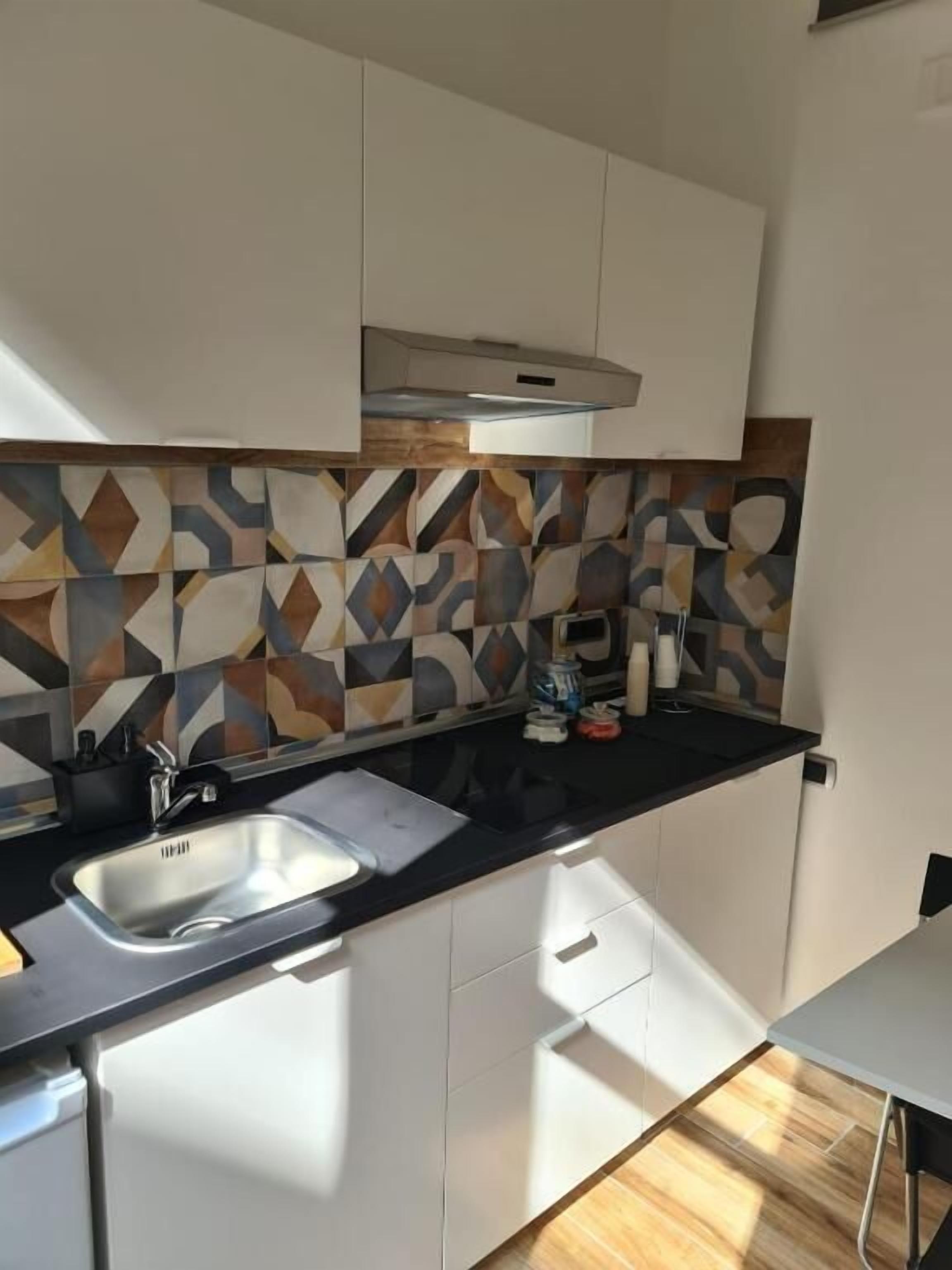 Una cocina moderna con encimera negra, armarios blancos y un salpicadero con estampado.
