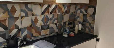 Una cocina moderna con encimera negra, armarios blancos y un salpicadero con estampado.