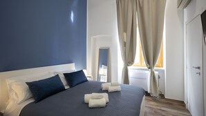 Ein Schlafzimmer mit einem großen Bett, einem Nachttisch, einer Lampe und einem Fenster mit Vorhängen.