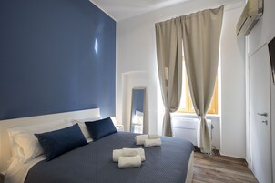 A bedroom with a large bed, a bedside table, a lamp, and a window with curtains.