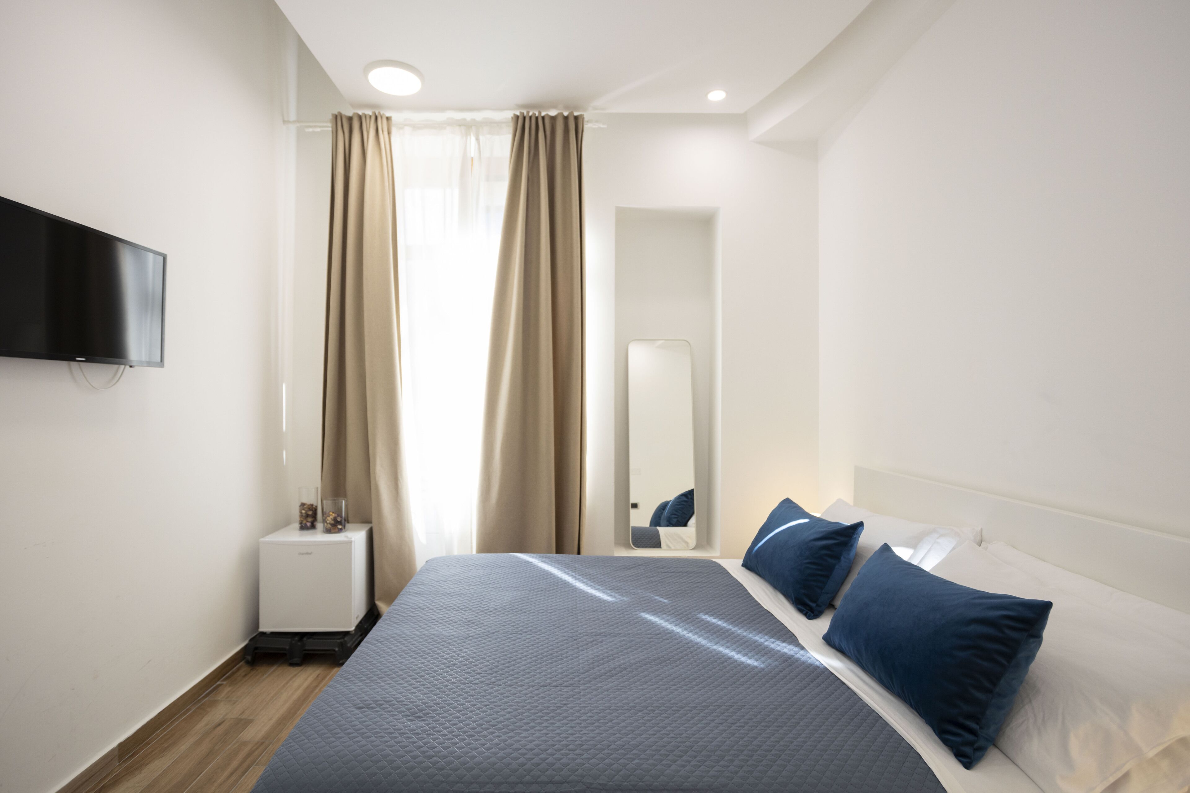 Ein modernes Hotelzimmer mit einem großen Bett, einem Flachbildfernseher, einem kleinen Nachttisch und einem Spiegel.