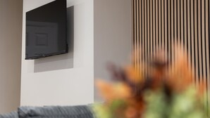 Una habitación con una pared blanca, televisor de pantalla plana montado, ventana con persianas verticales y un sofá.
