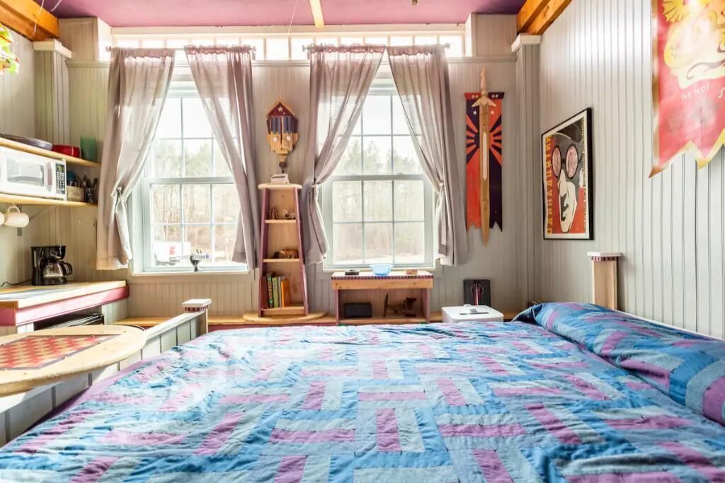 A bedroom with a bed, a desk, and a window with curtains.