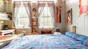 A bedroom with a bed, a desk, and a window with curtains.
