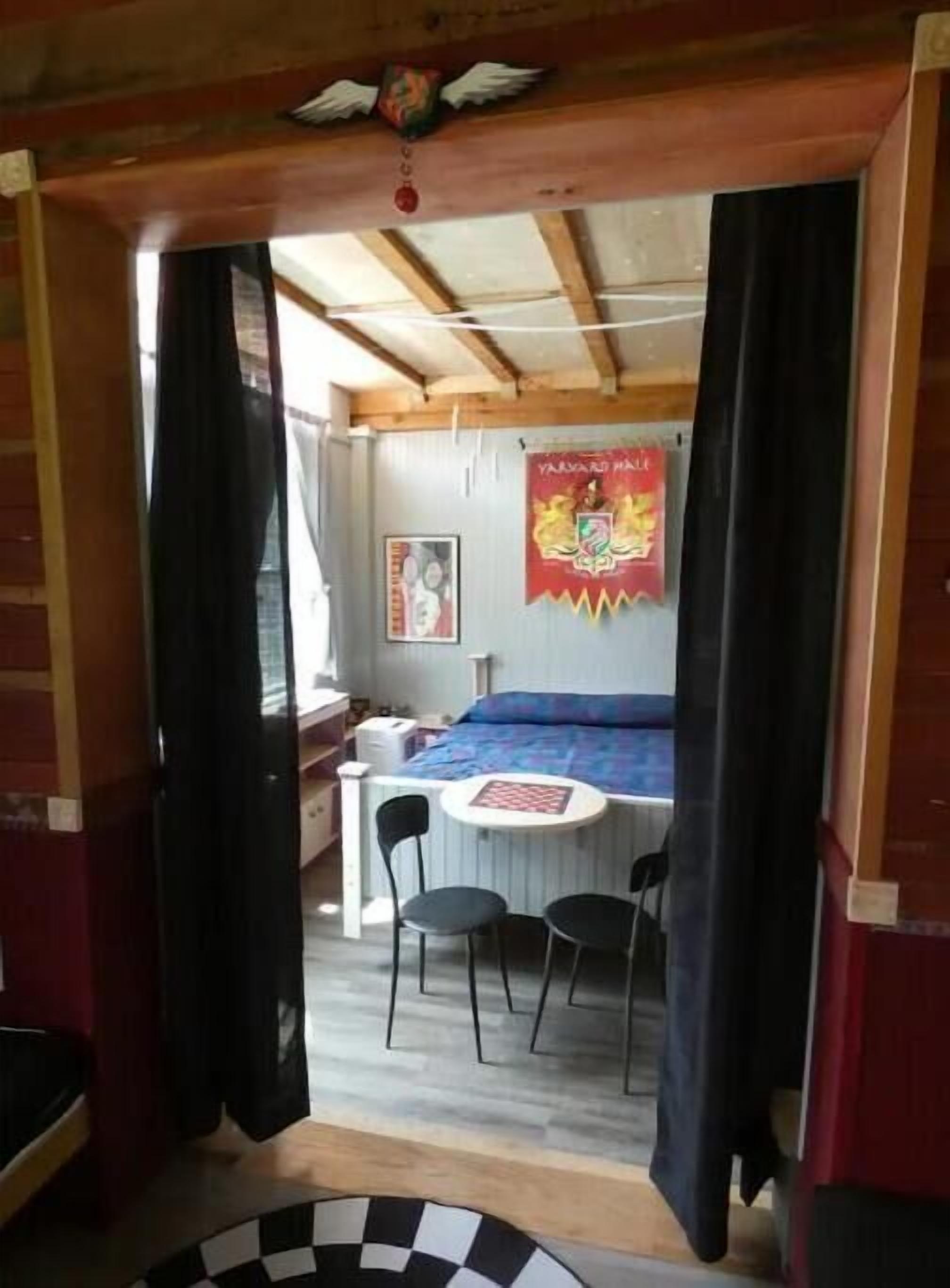 A room with a bed, a small table, two chairs, a window, and a poster on the wall.