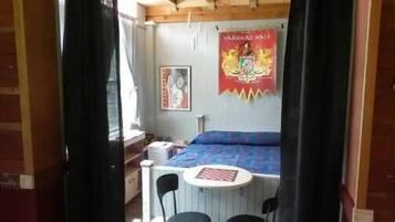 A room with a bed, a small table, two chairs, a window, and a poster on the wall.