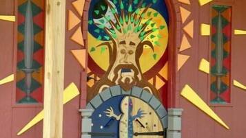 Entrada d'un edifici amb un mural colorit, un rellotge i una porta de fusta.
