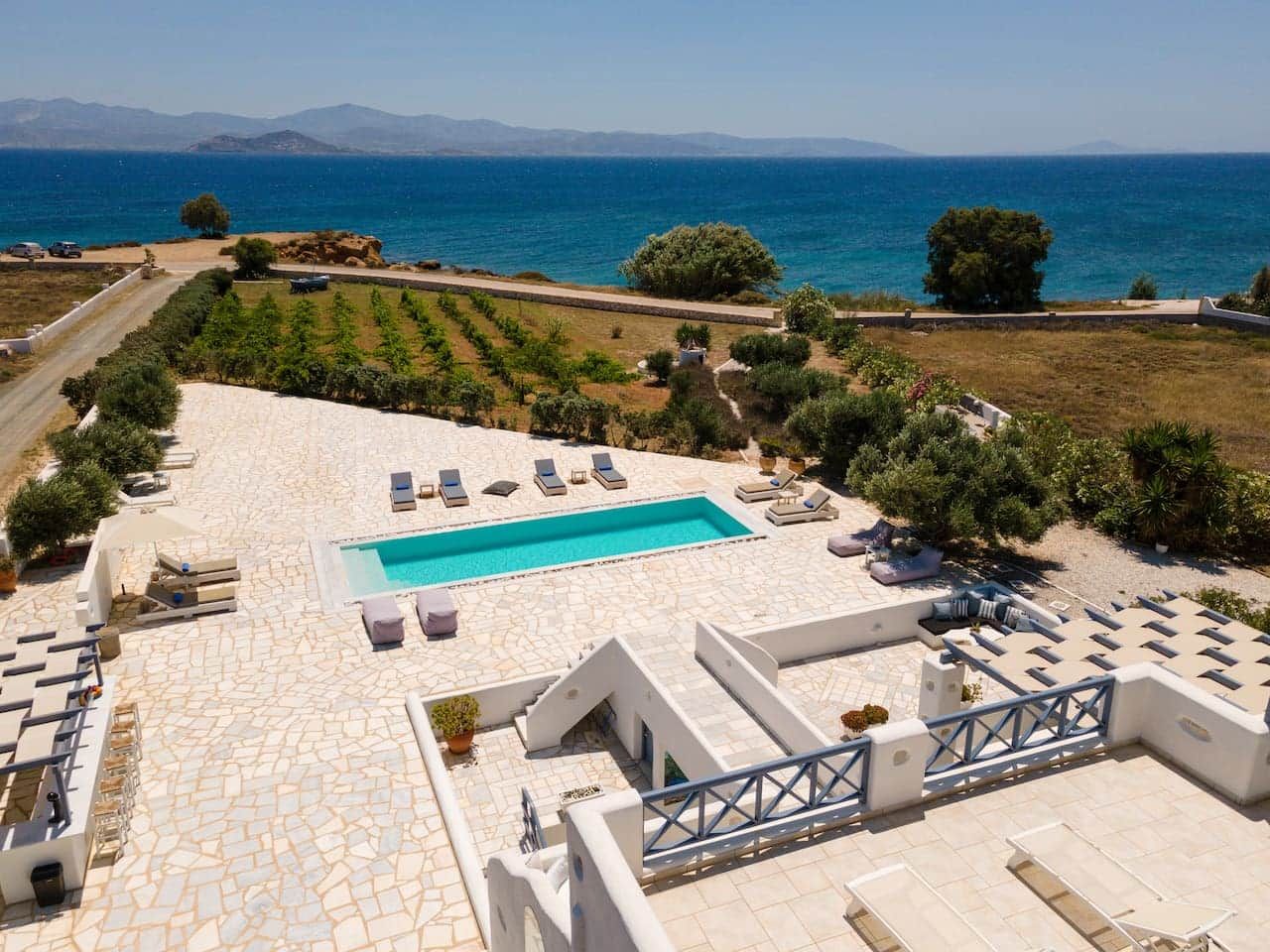Une piscine extérieure avec des chaises longues, entourée d’une terrasse en pierre et offrant une vue sur la mer.