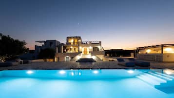 Una vila moderna amb piscina, mobiliari exterior i entrada ben il·luminada.