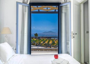 A hotel room with a bed, a view of the sea, and a balcony with a railing.