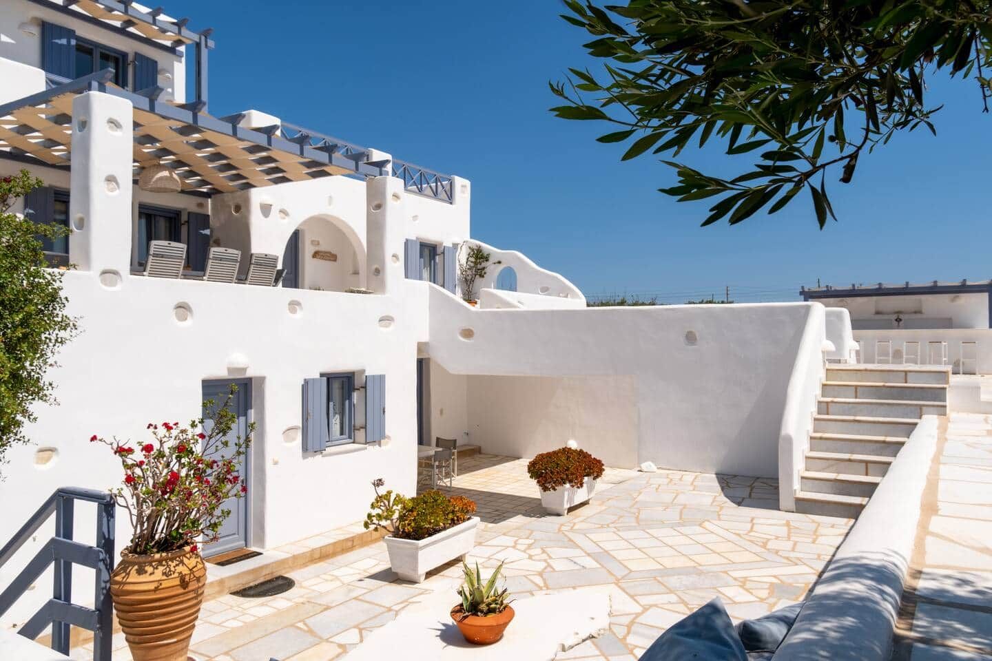 A white building with a balcony, potted plants, and a view of the sea.