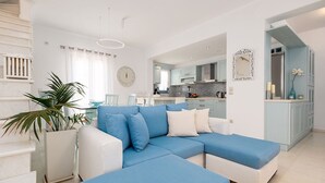 Uma sala de estar moderna com um sofá seccional azul, poltronas brancas e uma grande planta em vaso.