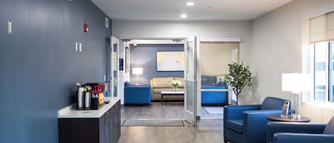 Un moderno vestíbulo de hotel con una pared azul, una recepción, un sofá, una mesa de centro y una planta.