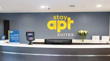 A reception desk with a 'stay apt SUITES' sign, a ViewSonic monitor, a payment terminal, and a vase with flowers.
