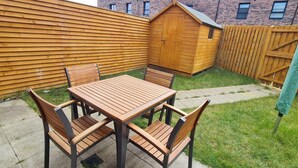 A patio with a wooden table and chairs, a wooden fence, and a shed in the background. - Pennywell 2 Bedroom House - Edinburgh  (Edinburgh)