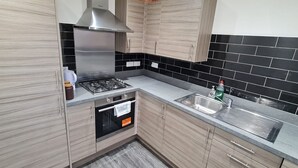 A modern kitchen with light wood cabinets, a stainless steel range hood, a gas stove, a built-in oven, and a black tiled backsplash. - Pennywell 2 Bedroom House - Edinburgh  (Edinburgh)