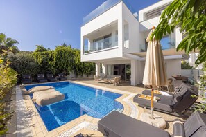 A modern two-story house with a swimming pool, outdoor seating, and lush greenery.