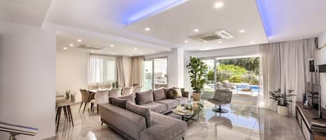 A modern living room with a grey sofa, a coffee table, and a dining area with chairs.