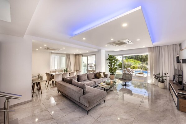 A modern living room with a grey sofa, a coffee table, and a dining area with chairs.