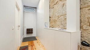 Un couloir étroit avec un plancher en bois, une porte blanche, un mur en pierre et une petite fenêtre.