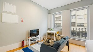 Un salon moderne doté d’un téléviseur à écran plat, d’un canapé, d’une petite table et d’une fenêtre donnant sur des immeubles.
