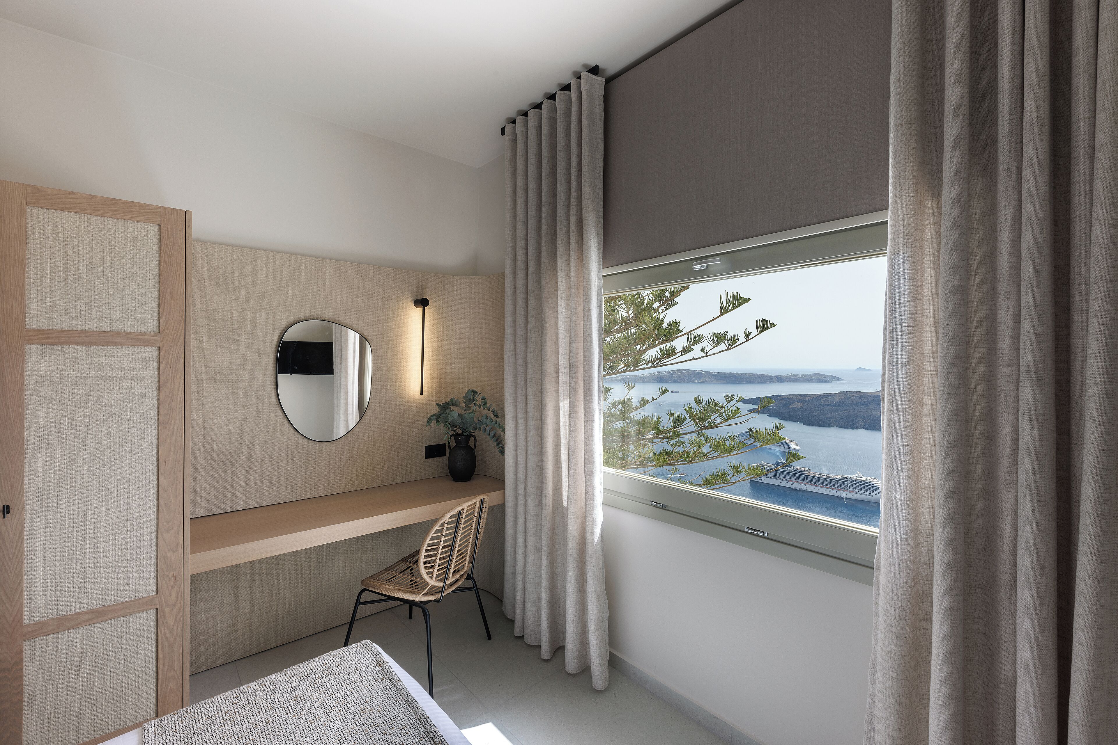 A modern bedroom with a view of a coastal landscape, a wooden desk, a chair, and a bedside table.