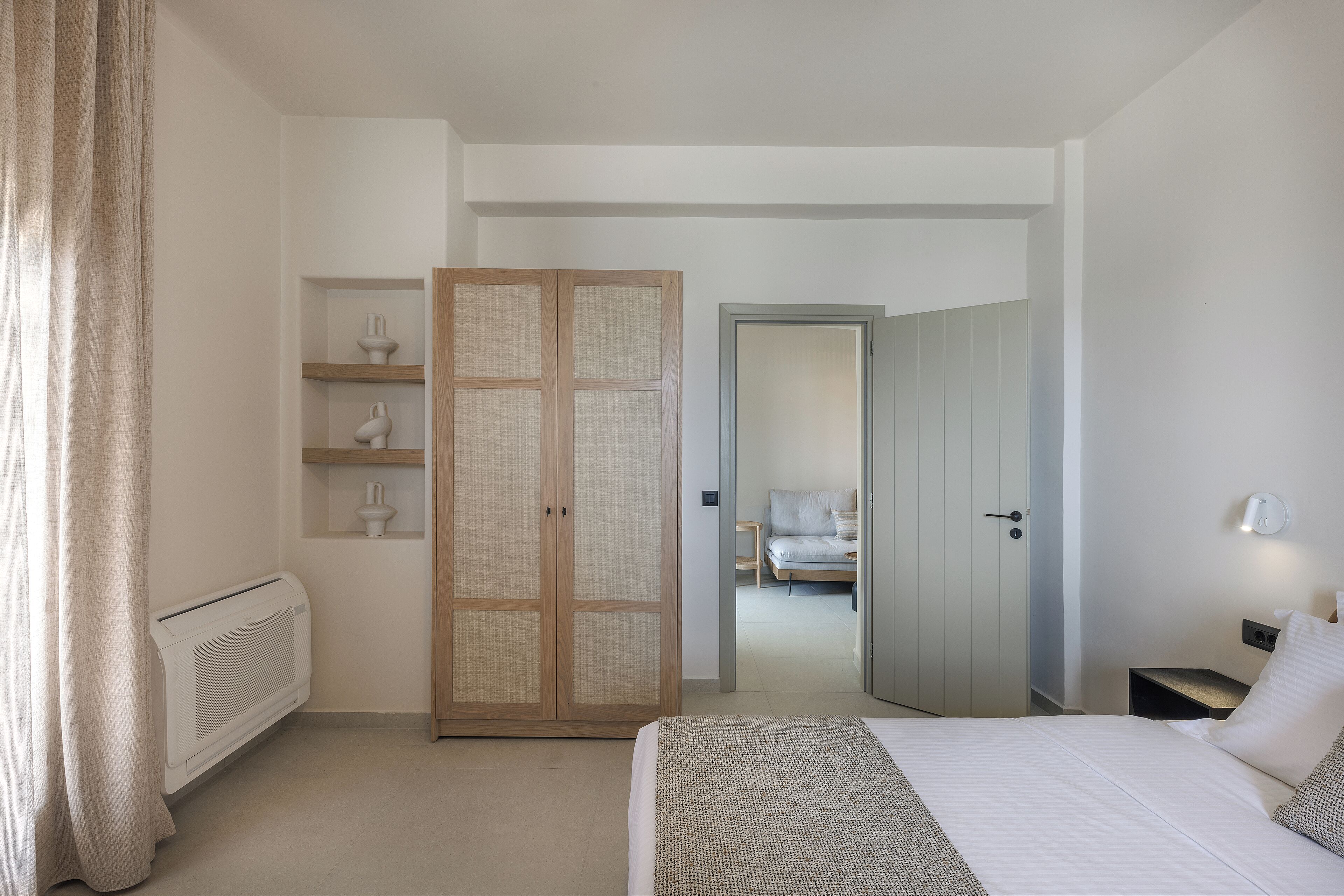 A hotel room with a bed, a wardrobe, a radiator, and a door leading to another room.