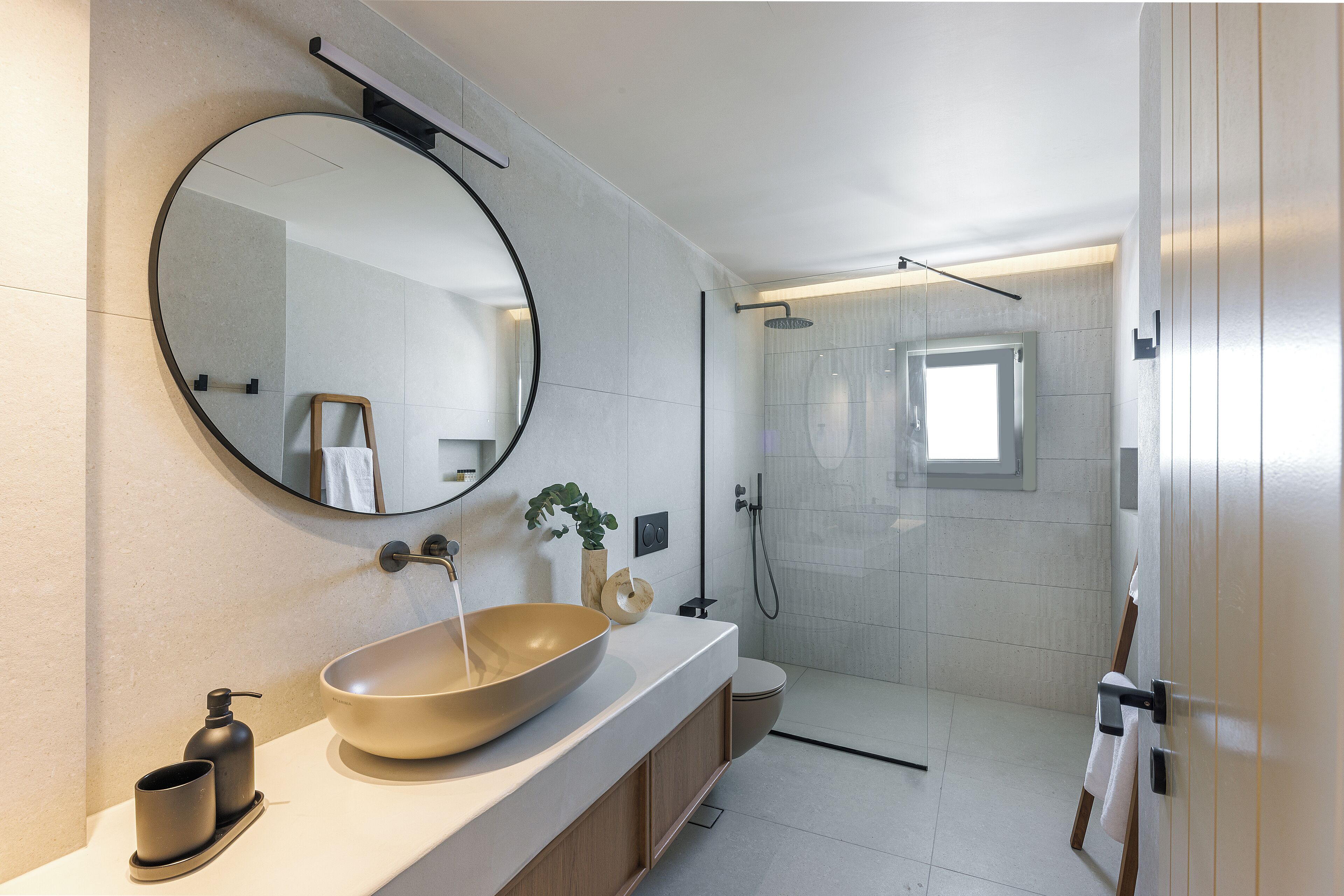 Un baño moderno con un espejo ovalado grande, un lavabo sobre encimera, un cabezal de ducha manual y un inodoro.
