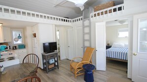 A compact, well-lit room with a dining area, a television, a wicker chair, and a bed with striped bedding. - Beachland K (Sandwich)