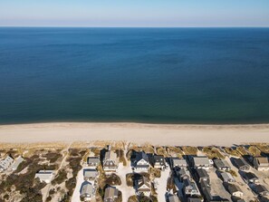Une zone résidentielle côtière où les maisons sont alignées le long du bord de mer, avec une plage de sable et l’océan en toile de fond.