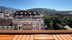 Un immeuble à plusieurs étages doté de balcons, un ciel dégagé et des montagnes en arrière-plan.