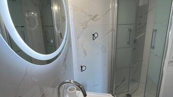 A bathroom with a modern sink, a round mirror, and a glass-enclosed shower.