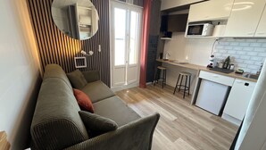 Un salon moderne avec un canapé, un miroir rond et un coin cuisine équipé d’un four à micro-ondes, d’un évier et de tabourets.