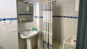 A bathroom with a white sink, a mirror, a shower with a patterned curtain, and a white shelf. - Hostal Avenida by Bossh! Hotels (Chipiona)