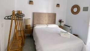 A bedroom with a bed, wooden hanger rack, bedside lamp, and a small table with a vase of flowers. - Hostal Avenida by Bossh! Hotels (Chipiona)