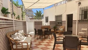 An outdoor patio with checkered flooring, wicker furniture, and tiled walls. - Hostal Avenida by Bossh! Hotels (Chipiona)