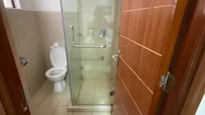 A small bathroom with a toilet, a glass shower enclosure, and a wooden door. - Riverside Homes 6C (Nairobi)