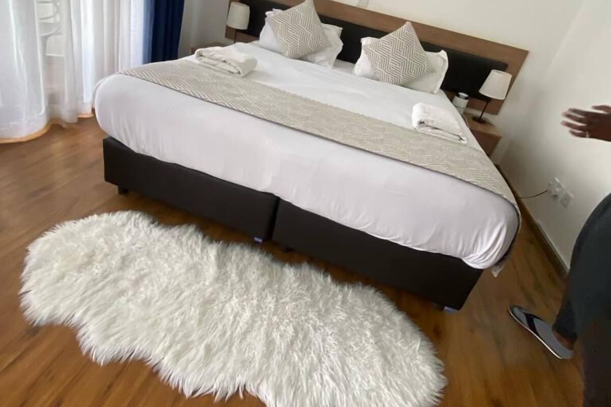 A hotel room with a large bed, a fluffy white rug, and a painting on the wall.