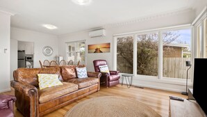 A living room with a brown leather sofa, a red leather chair, and a dining area with white cabinets and a microwave.